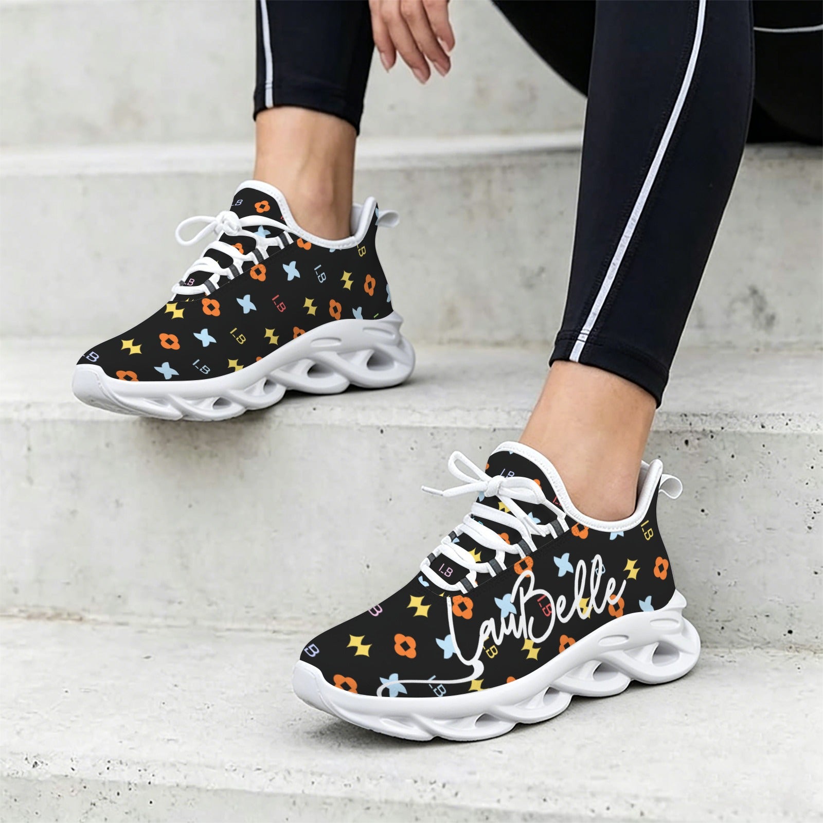 Black sneakers with colorful patterns, white laces, and chunky white soles on a concrete step.