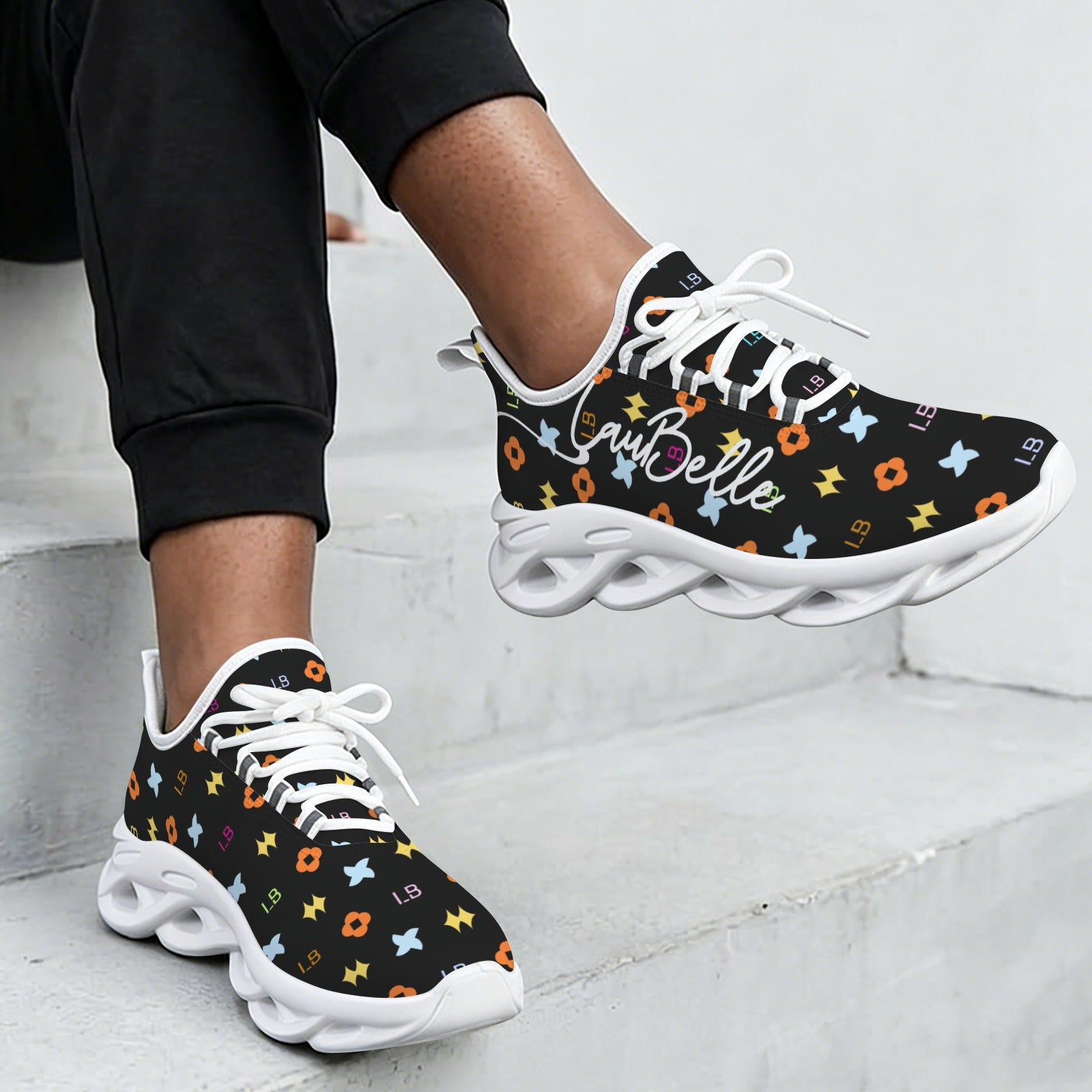 Black sneakers with colorful patterns and white laces, on a person sitting on concrete steps.