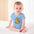 Baby in blue onesie with cartoon bear design sitting on a white blanket.