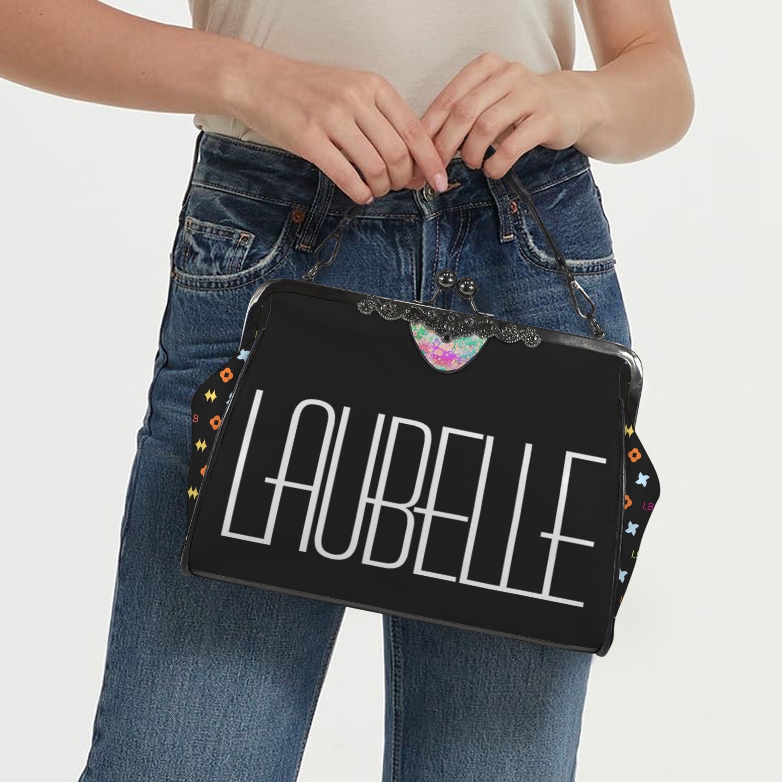 Person holding a black clutch with "LAUBELLE" text, colorful patterns, and wearing blue jeans.
