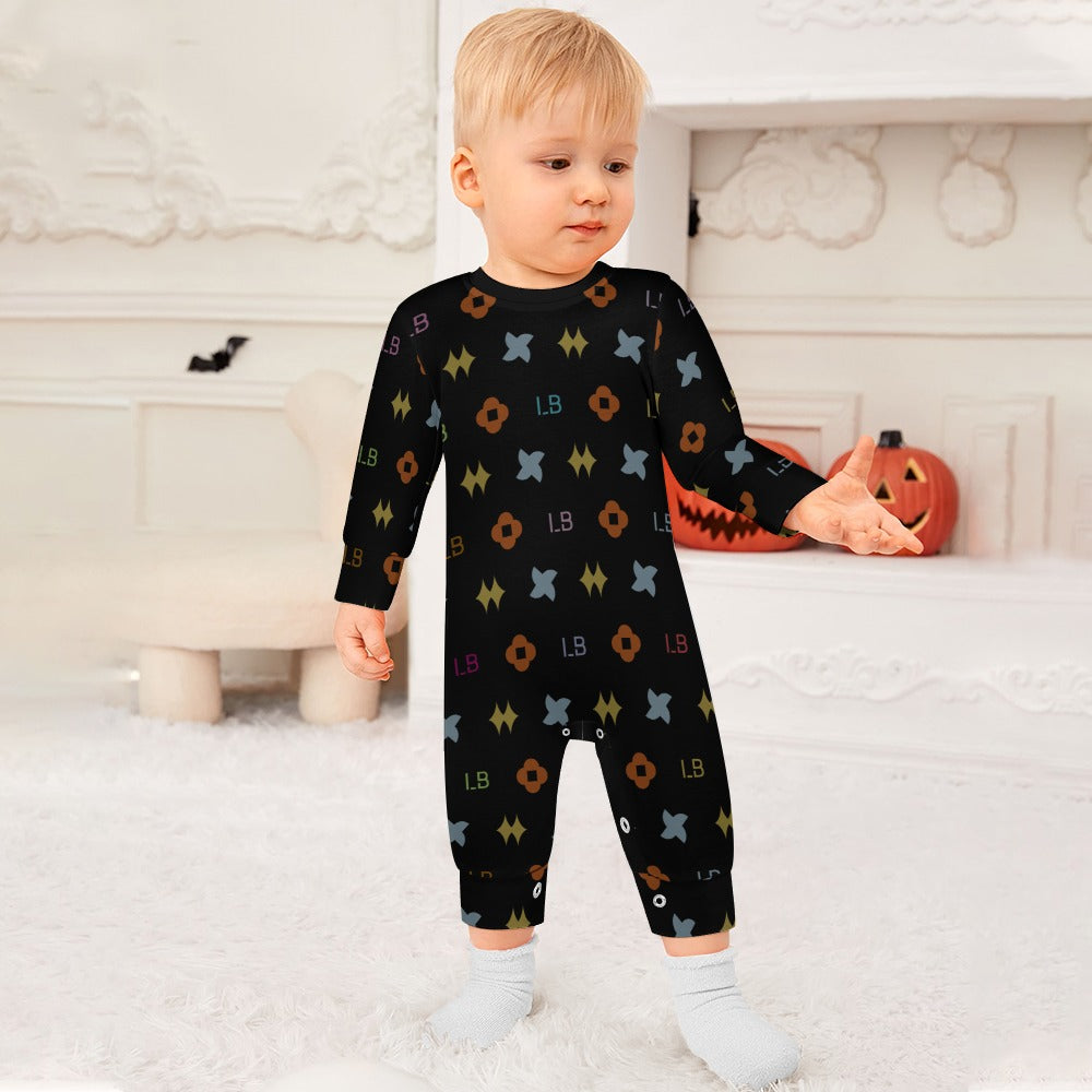Toddler in a black patterned onesie stands on a white rug with pumpkin decorations behind.