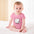 Baby in a pink onesie with a cute cartoon cat design, sitting on a white blanket.